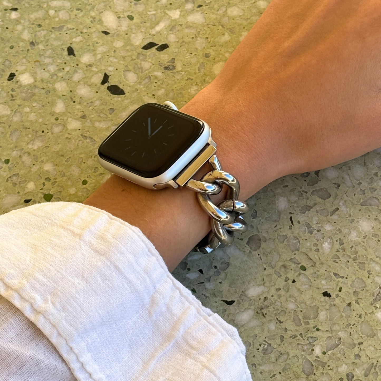Smartwatch on a wrist with a chain strap against a textured surface