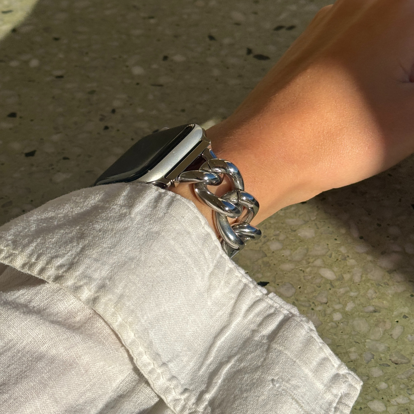 Person wearing a smartwatch with a chain bracelet on a concrete surface