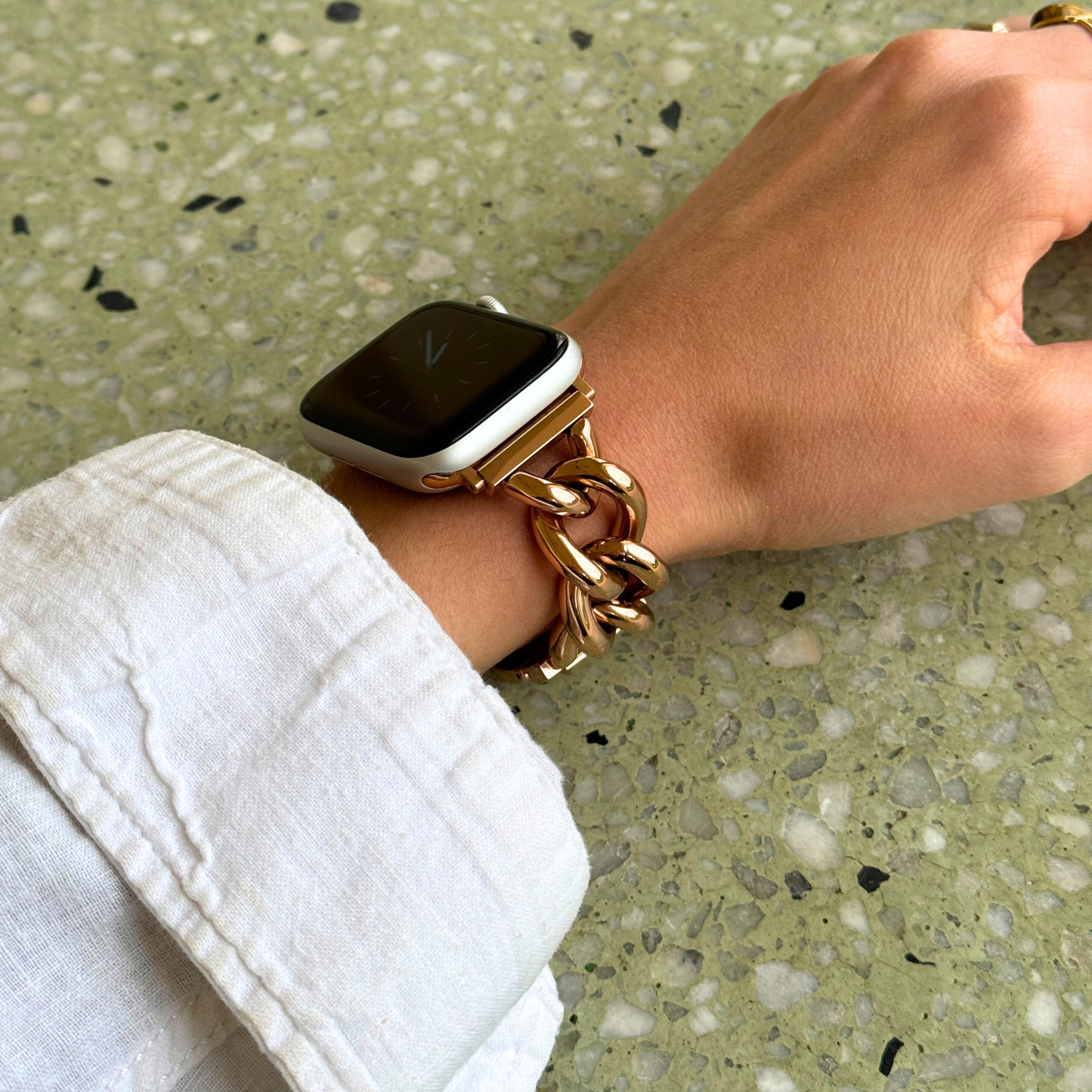Hand wearing a gold chain watch on a textured surface
