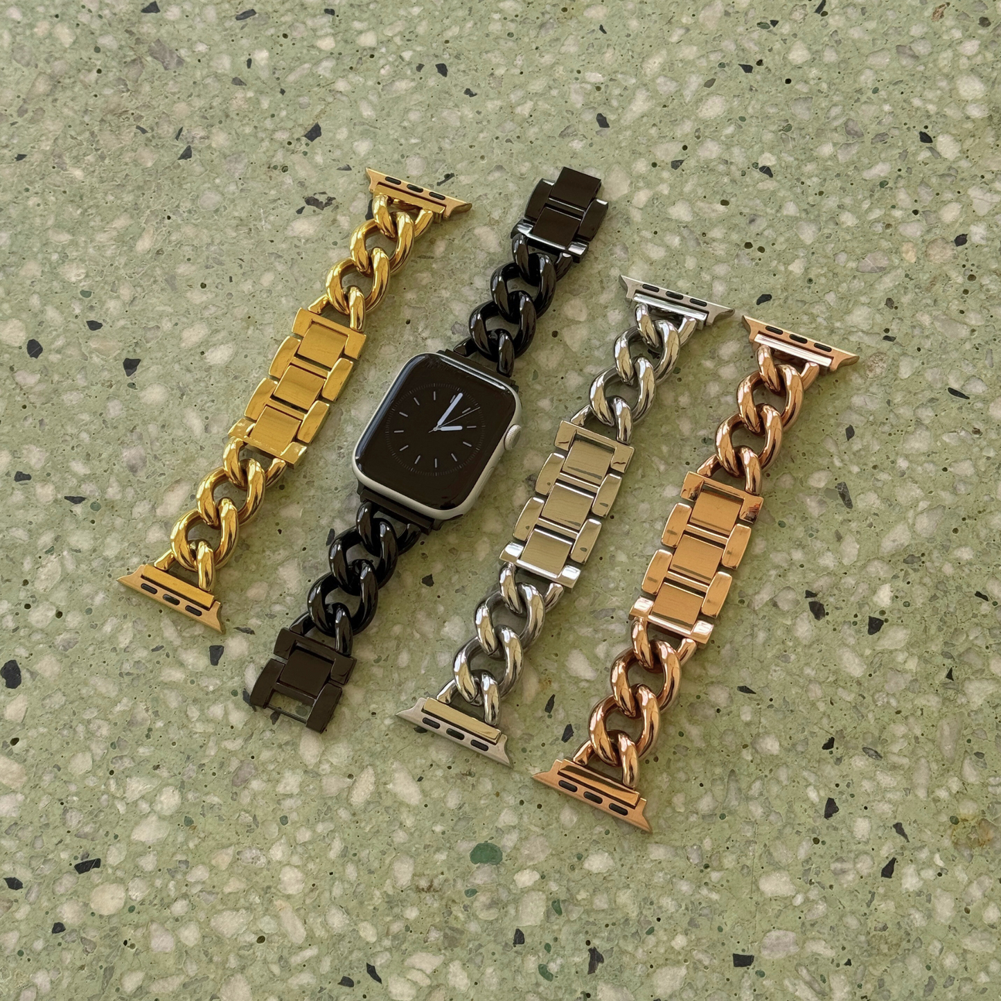 Four gold chain watch straps on a textured green surface