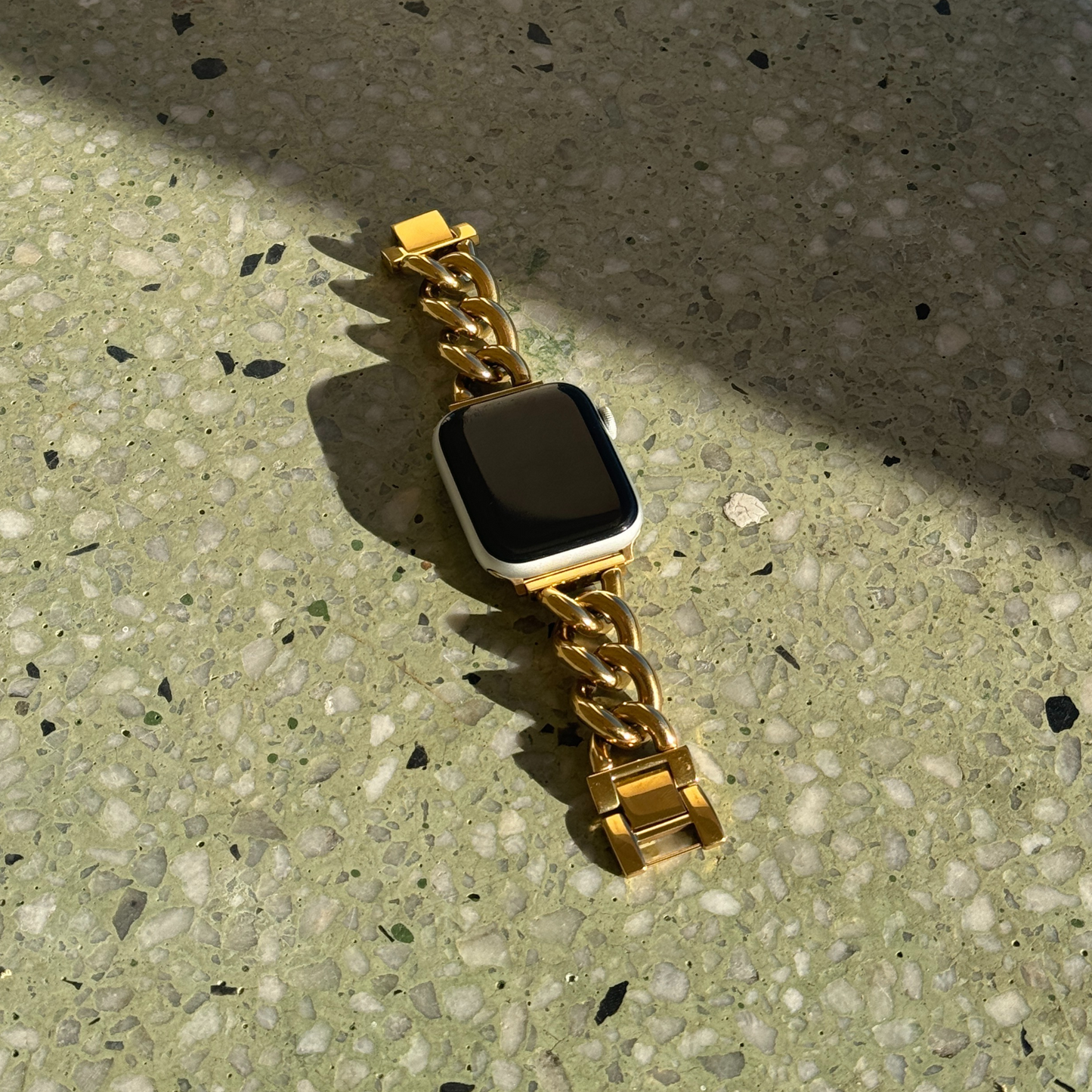 Smartwatch with a gold chain strap on a textured surface