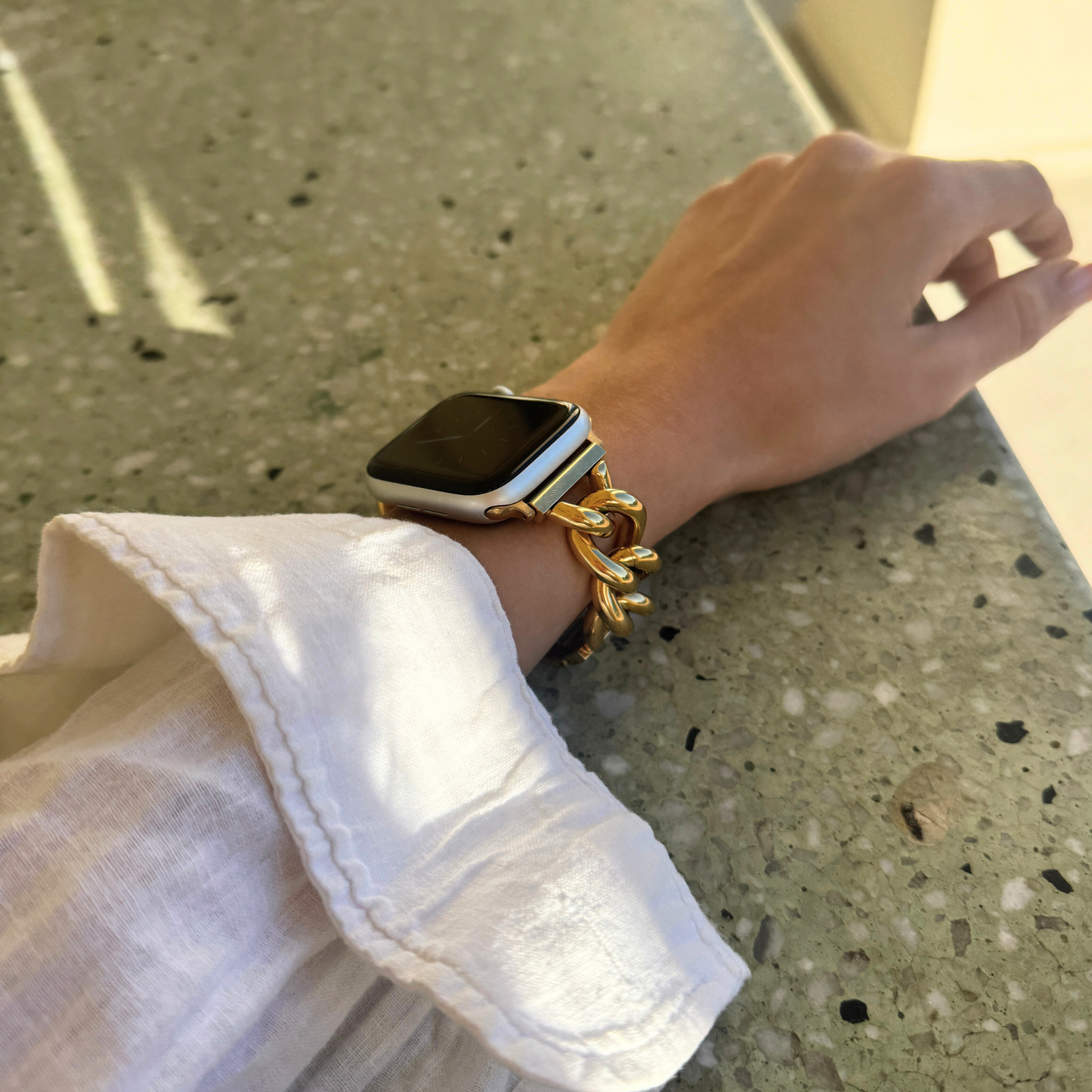 Hand wearing a smartwatch and gold bracelet on a concrete surface