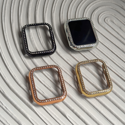 Four square-shaped watch cases in black, silver, rose gold, and gold on a textured light gray surface.