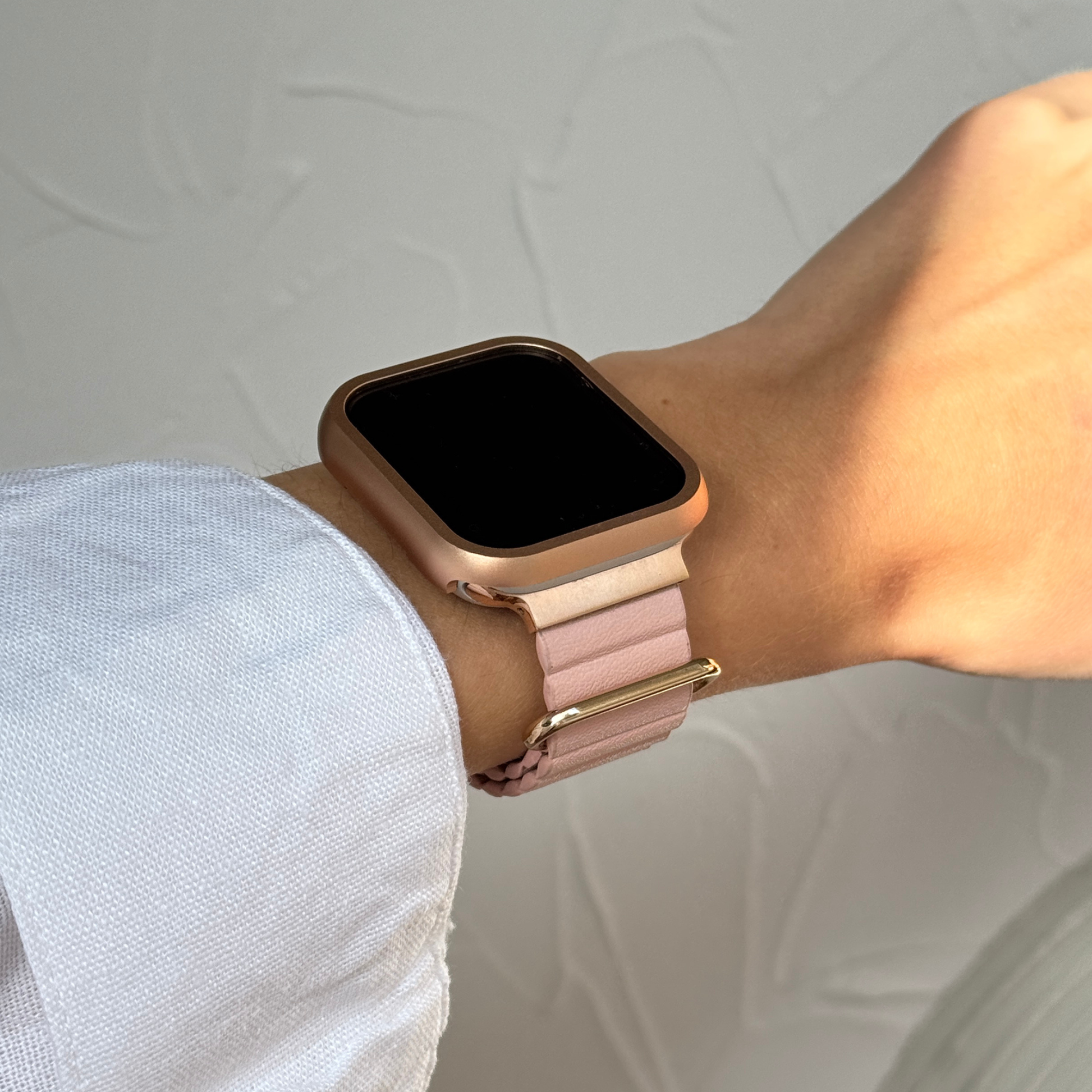 Smartwatch with a rose gold case and pink band on a wrist against a neutral background
