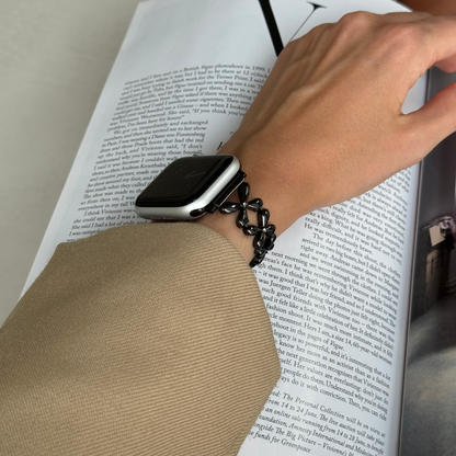 Black floral link Apple Watch band worn with a camel sleeve over a book page, metal strap for Apple Watch 38mm to 49mm