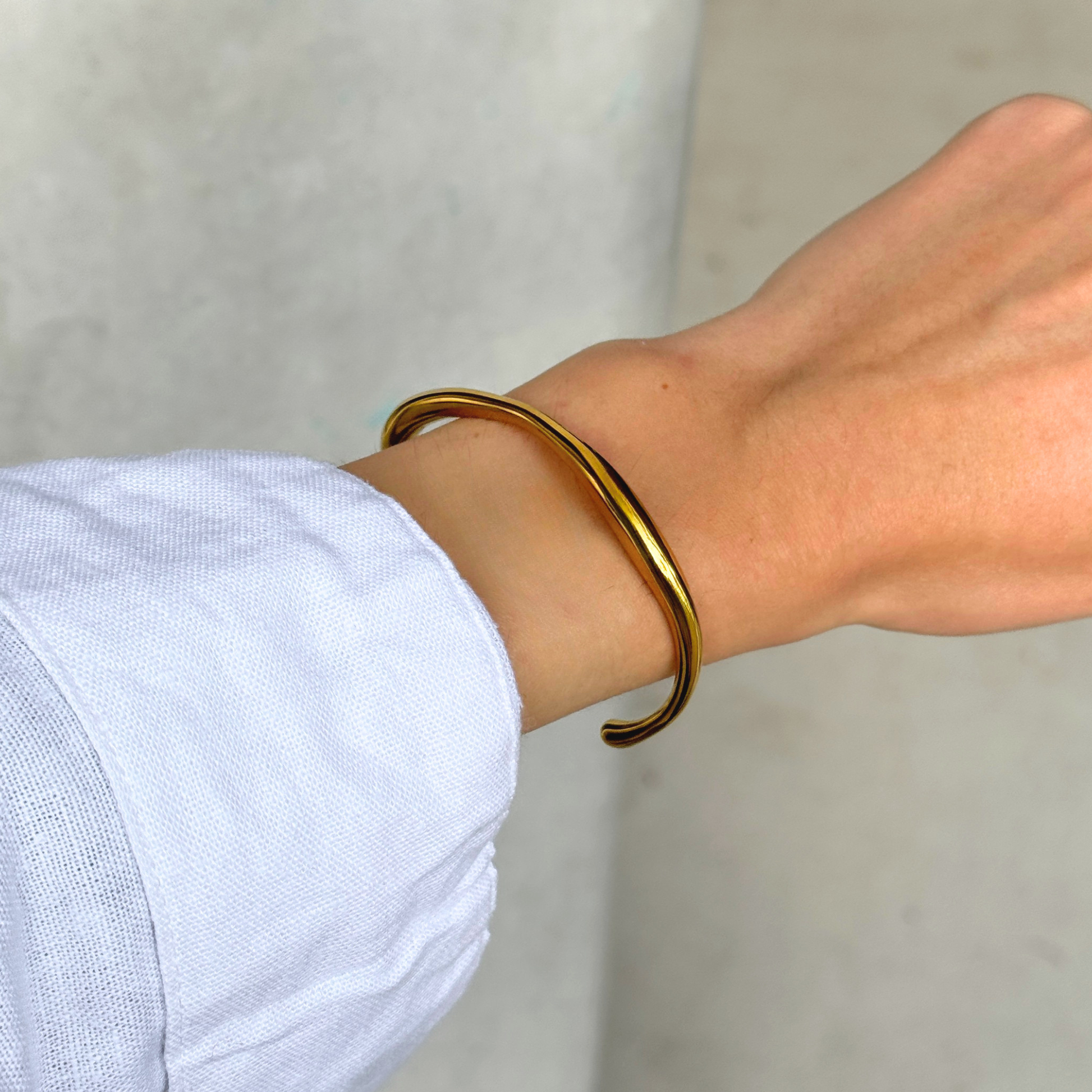 A polished gold-toned metal cuff bracelet worn on a person's wrist, shown against a neutral light gray background.