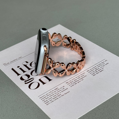 Rose gold floral link Apple Watch band propped upright on a printed card, metal bracelet for Apple Watch 38mm to 49mm
