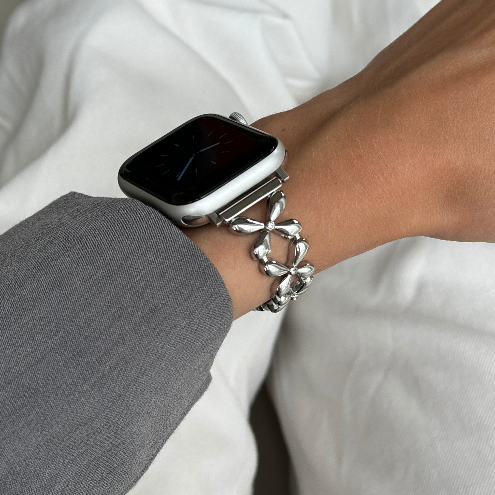 Silver floral link Apple Watch band worn on a wrist with a grey sleeve, metal strap for Apple Watch 38mm to 49mm