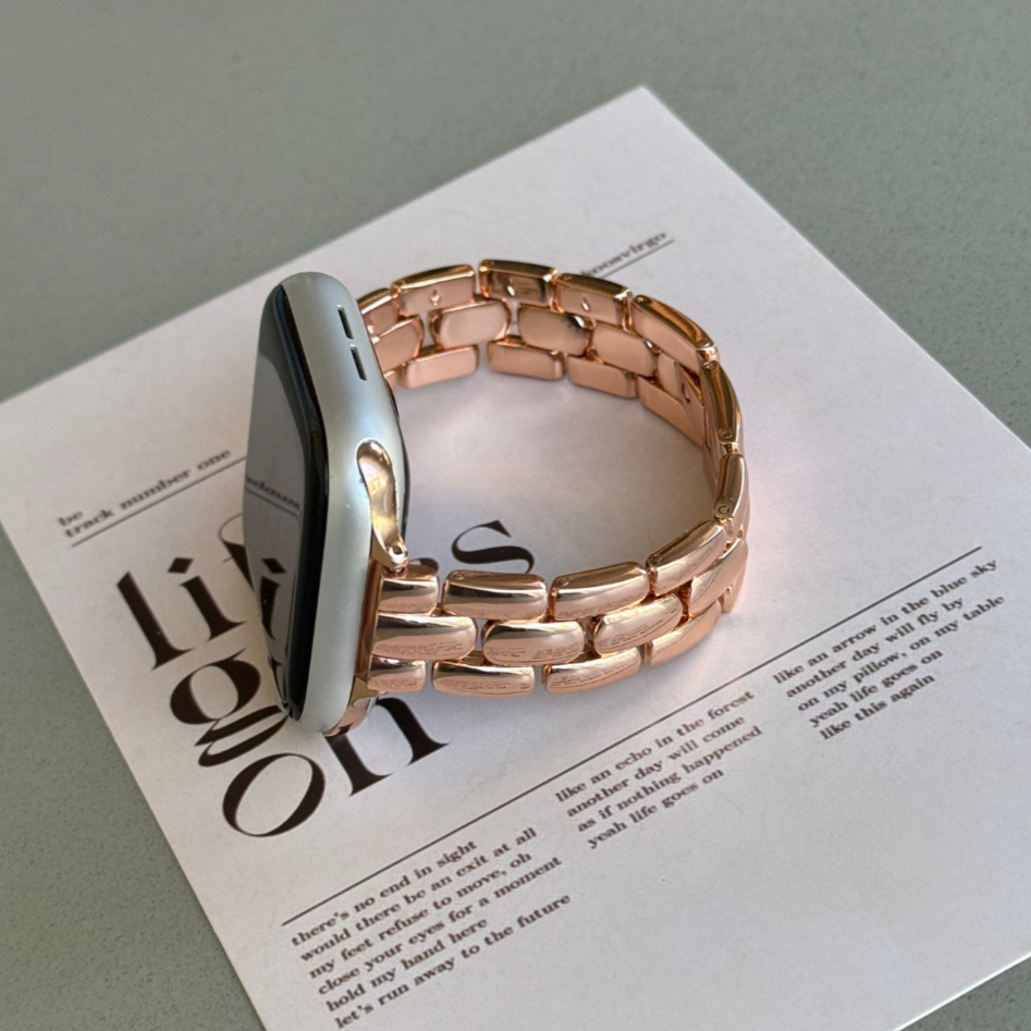 Rose gold slim link Apple Watch band propped on a printed page, metal strap for Apple Watch 38mm, 40mm, 41mm, 42mm, 44mm, 45mm, 46mm and 49mm