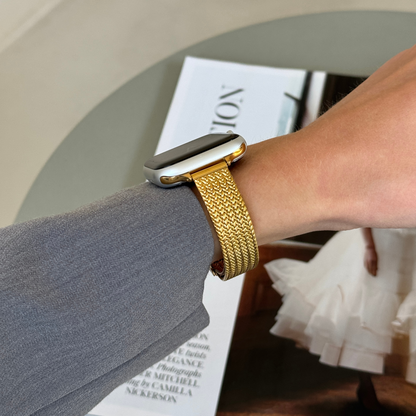 Gold woven mesh Apple Watch band worn on a wrist beside an open magazine, stainless steel strap for Apple Watch 38mm to 49mm