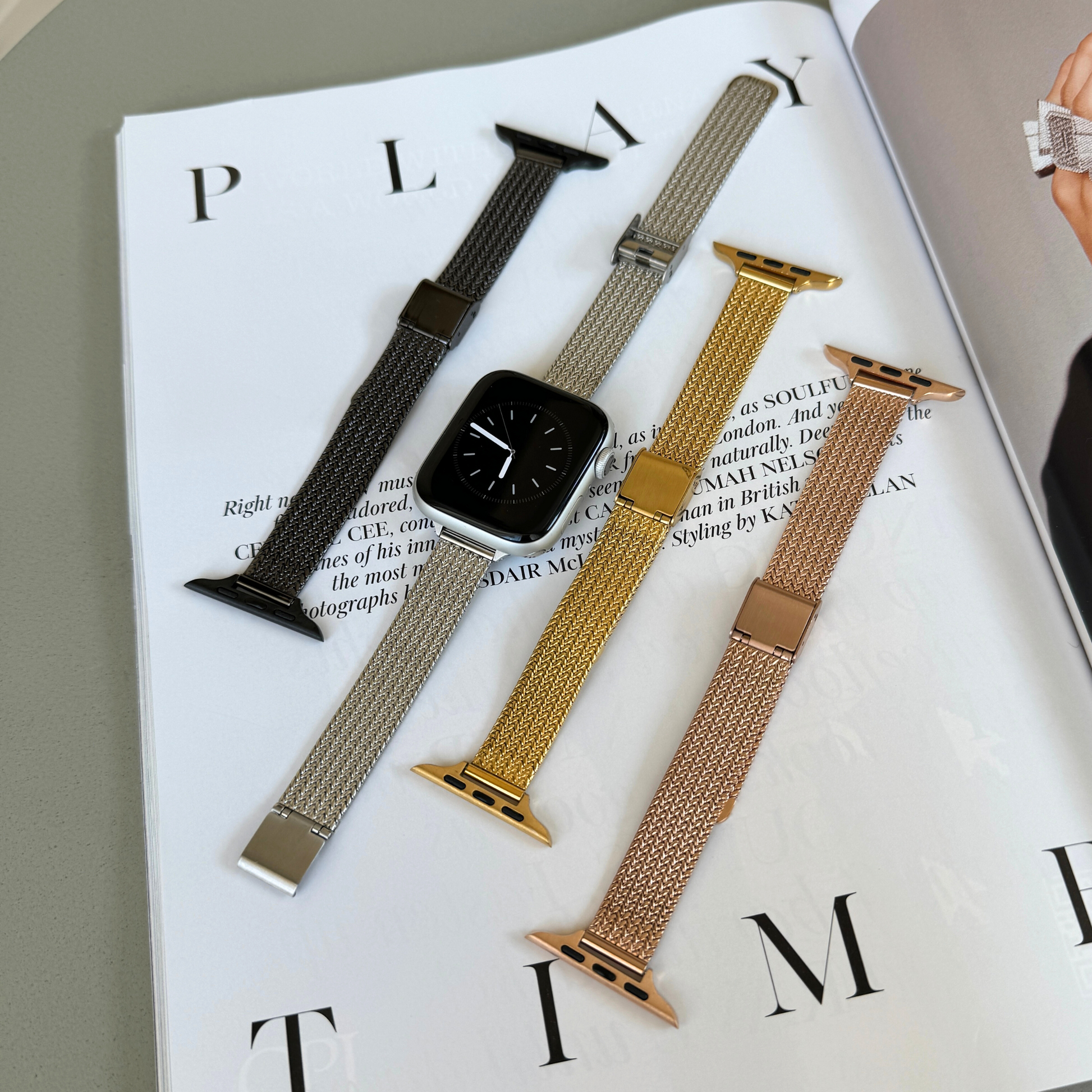 Black, silver, gold and rose gold woven mesh Apple Watch bands laid out on a magazine, stainless steel straps for Apple Watch 38mm to 49mm