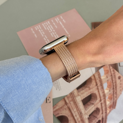 Rose gold woven mesh Apple Watch band worn on a wrist over a travel magazine, metal strap for Apple Watch 38mm to 49mm