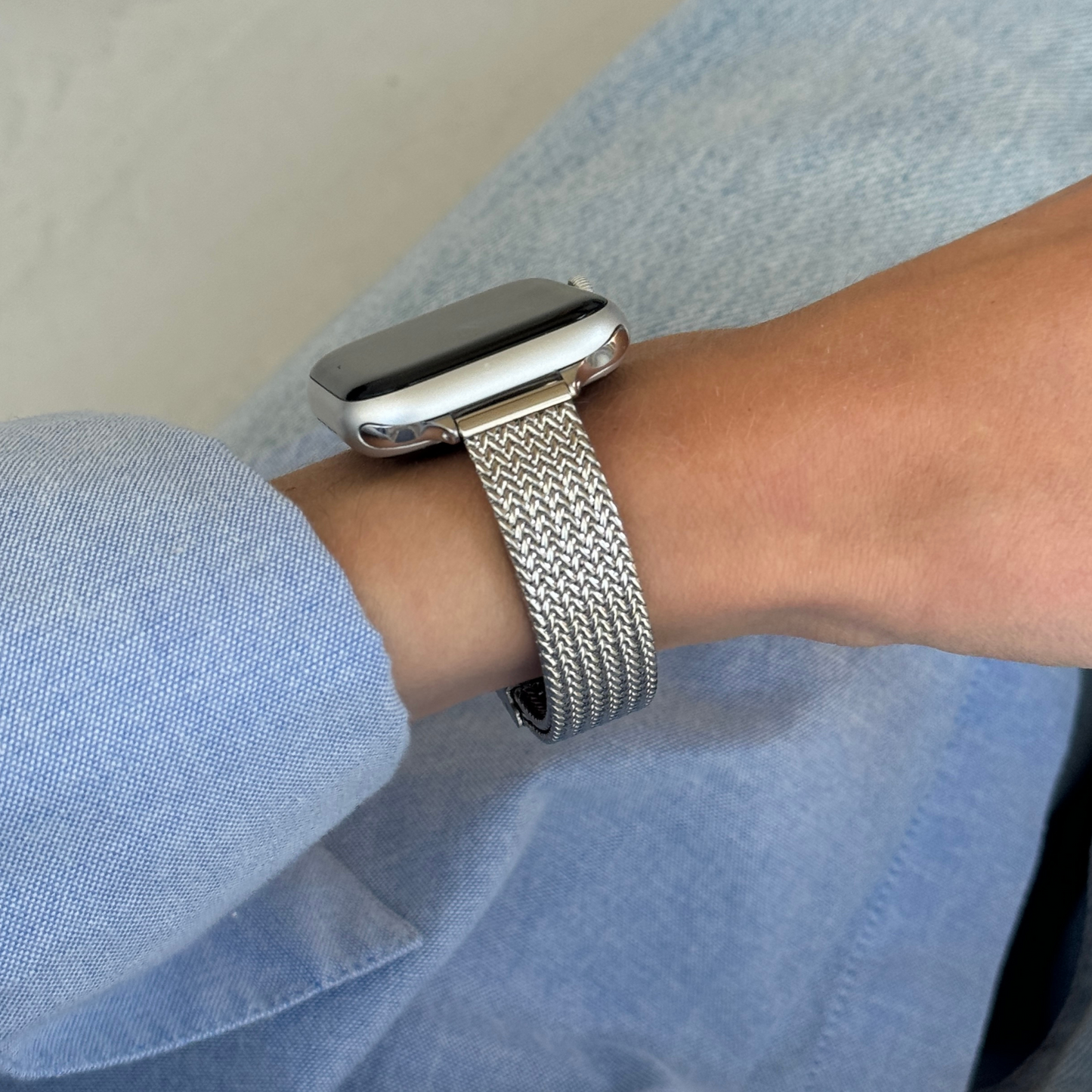 Silver woven mesh Apple Watch band worn on a wrist with a blue shirt cuff, stainless steel bracelet for Apple Watch 38mm to 49mm