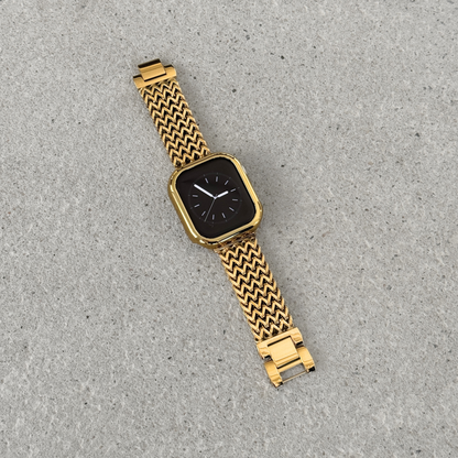 Apple Watch with a gold bumper case cover and a woven metallic mesh strap, photographed diagonally on a textured gray surface.