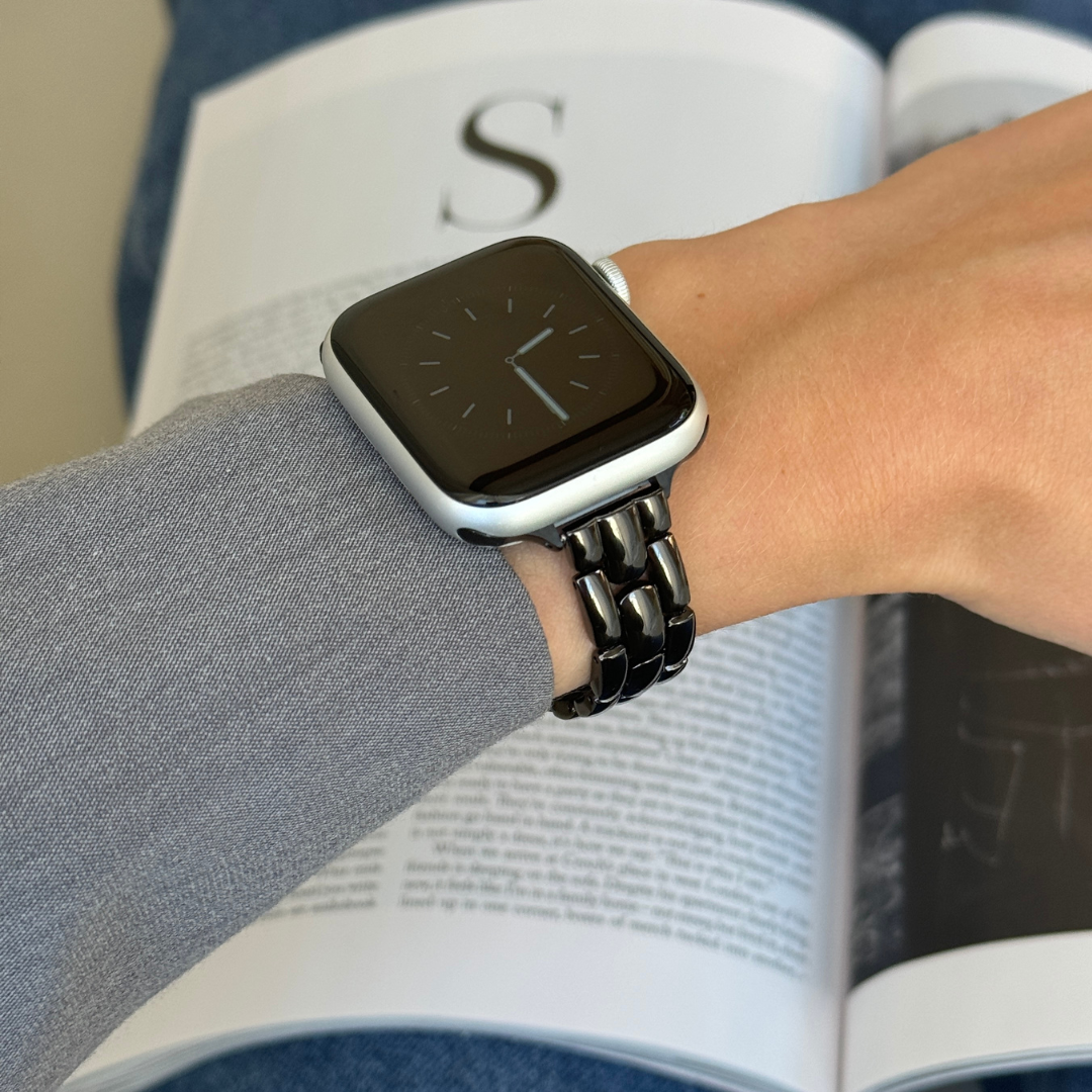 Black slim link Apple Watch band worn on a wrist against a blue cushion, metal bracelet for Apple Watch 38mm to 49mm