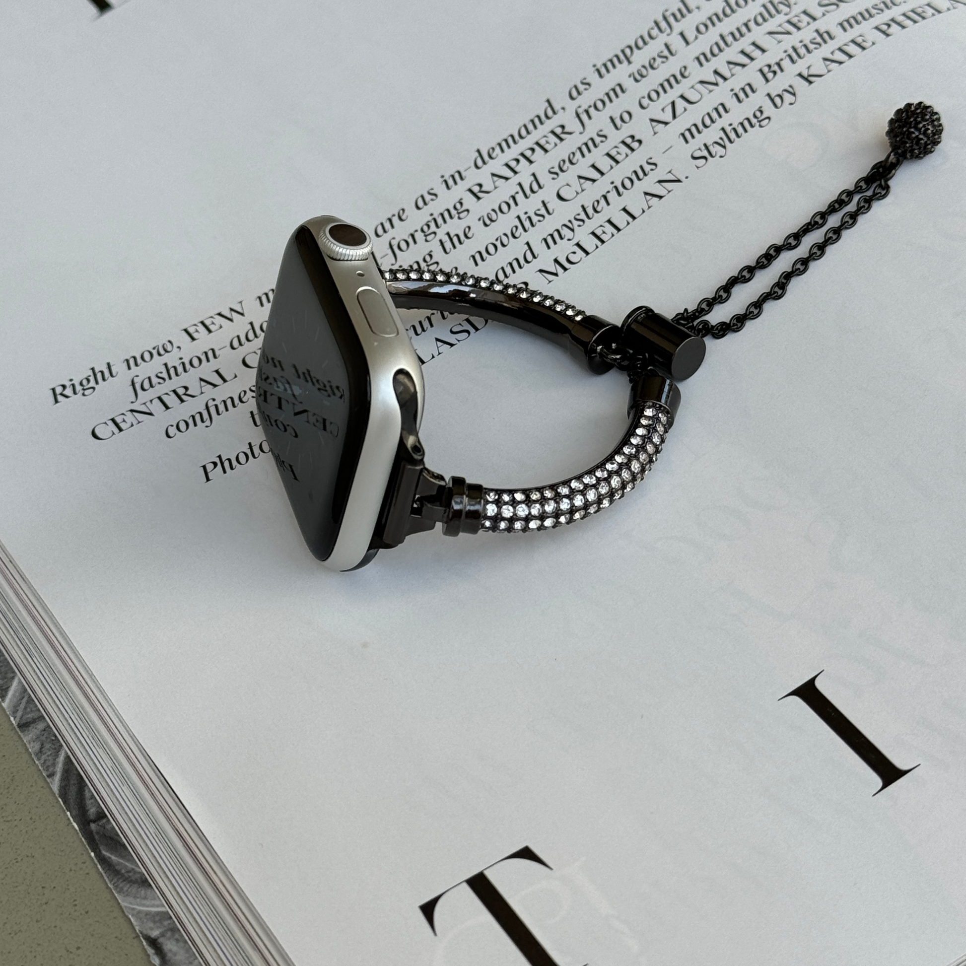 Black rhinestone Apple Watch band lying flat on an open magazine, metal bracelet for Apple Watch 38mm to 49mm