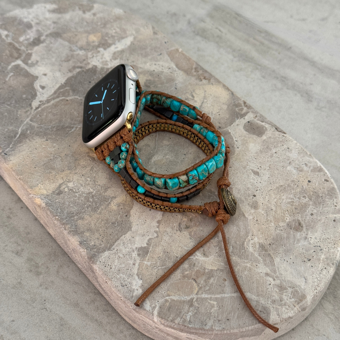 Smartwatch with a turquoise and brown wrap-around band on a stone surface