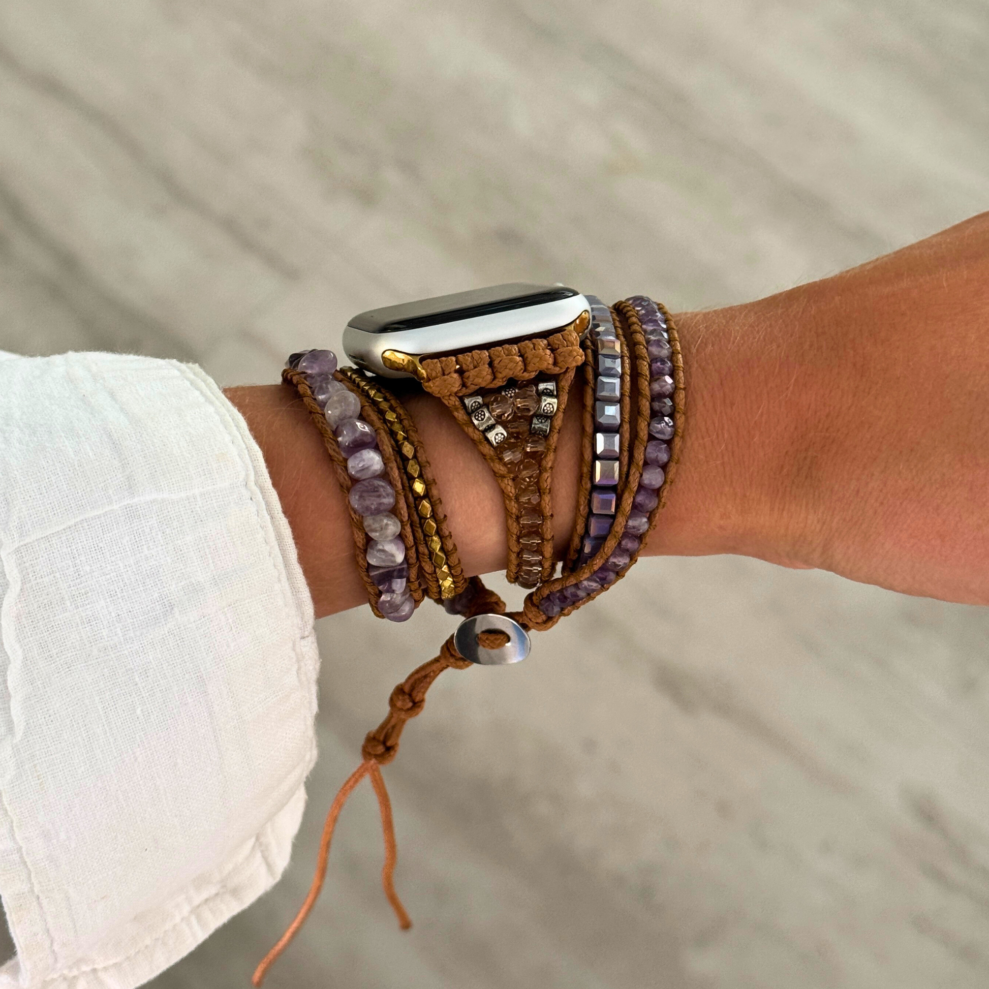 Person wearing a smartwatch with multiple bracelets on a neutral background