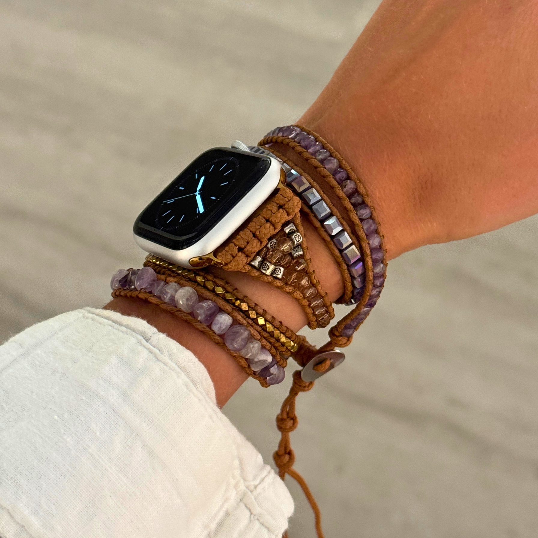 Person wearing a smartwatch with a braided rope and bead bracelet on a blurred natural background