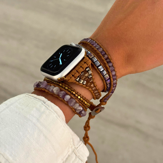 Person wearing a smartwatch with a braided rope and bead bracelet on a blurred natural background