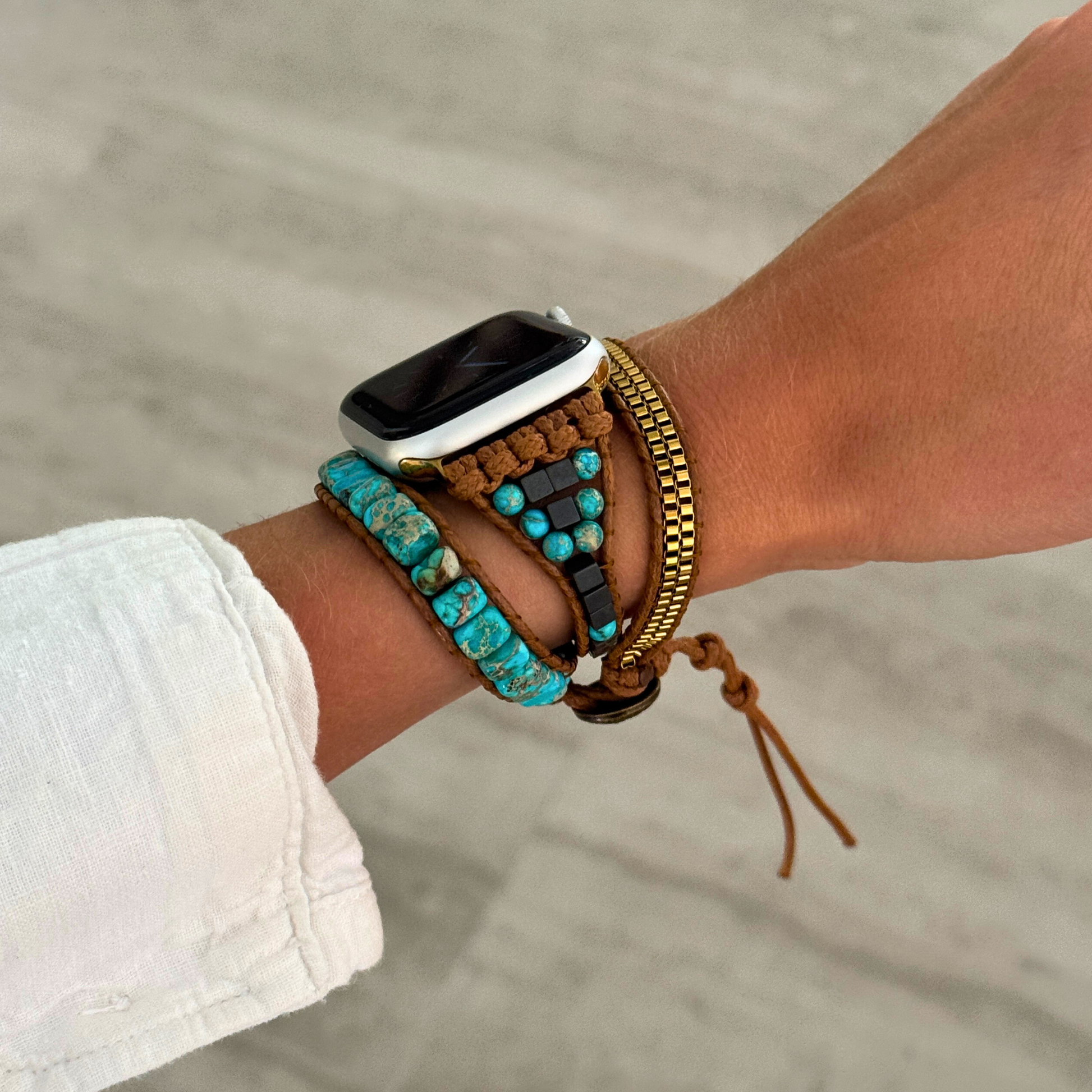 Wrist with multiple bracelets and a smartwatch on a blurred background