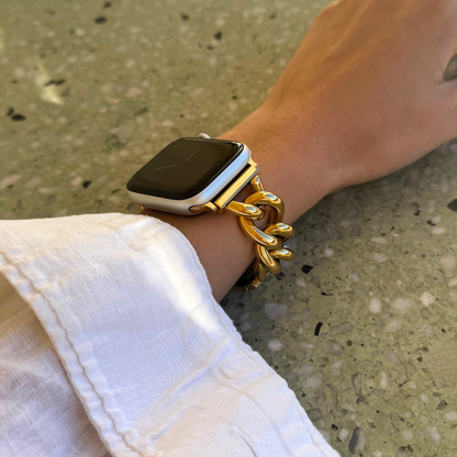 Smartwatch on a wrist with a gold chain bracelet against a concrete background
