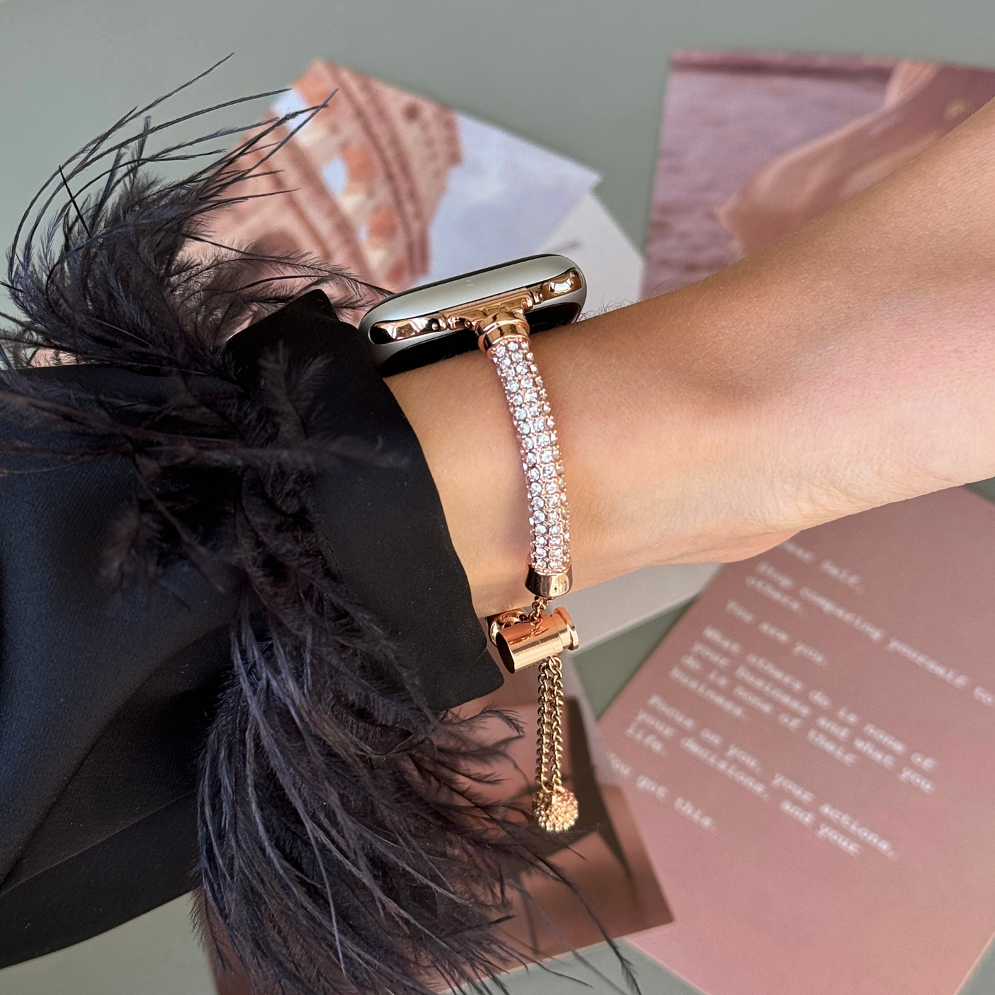 Rose gold rhinestone Apple Watch band worn on a wrist beside pink magazine pages, metal bracelet for Apple Watch 38mm to 49mm