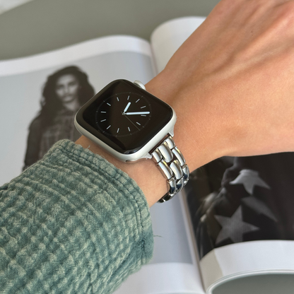 Silver slim link Apple Watch band worn with a green knit sleeve beside a magazine, metal bracelet for Apple Watch 38mm to 49mm