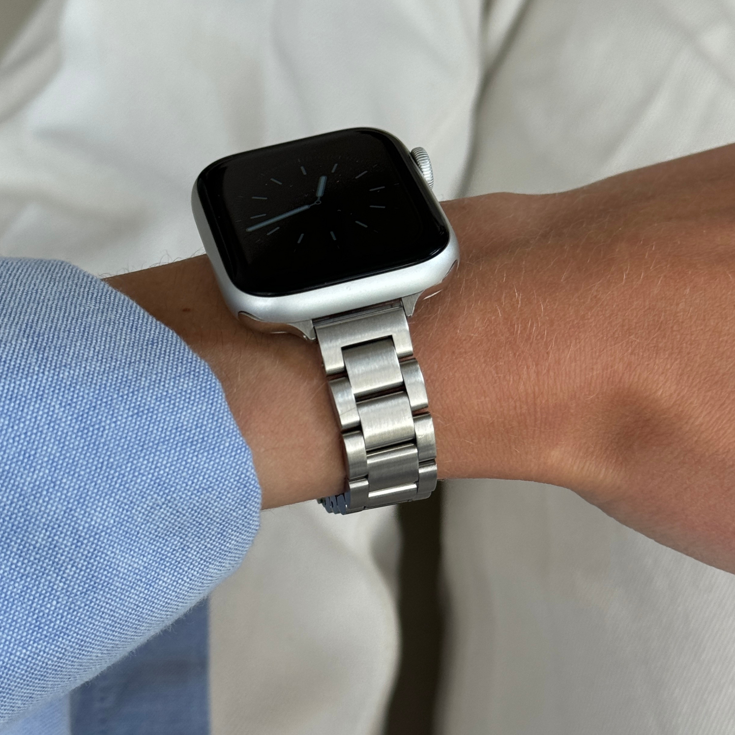 Silver slim link Apple Watch band worn on a wrist with a blue shirt cuff, stainless steel strap for Apple Watch 38mm to 49mm