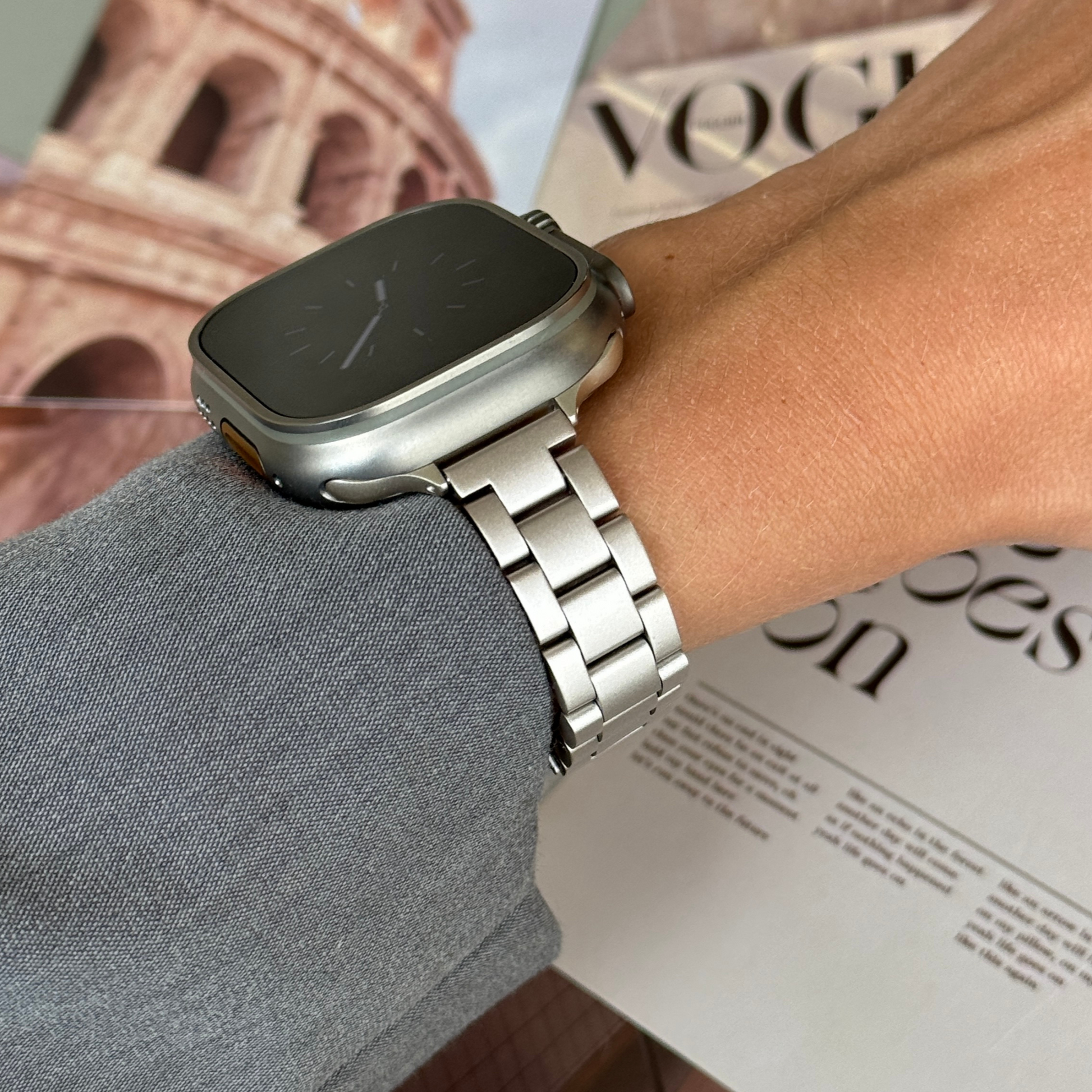 Starlight slim link Apple Watch band worn on a wrist above a travel poster, stainless steel bracelet for Apple Watch 38mm to 49mm