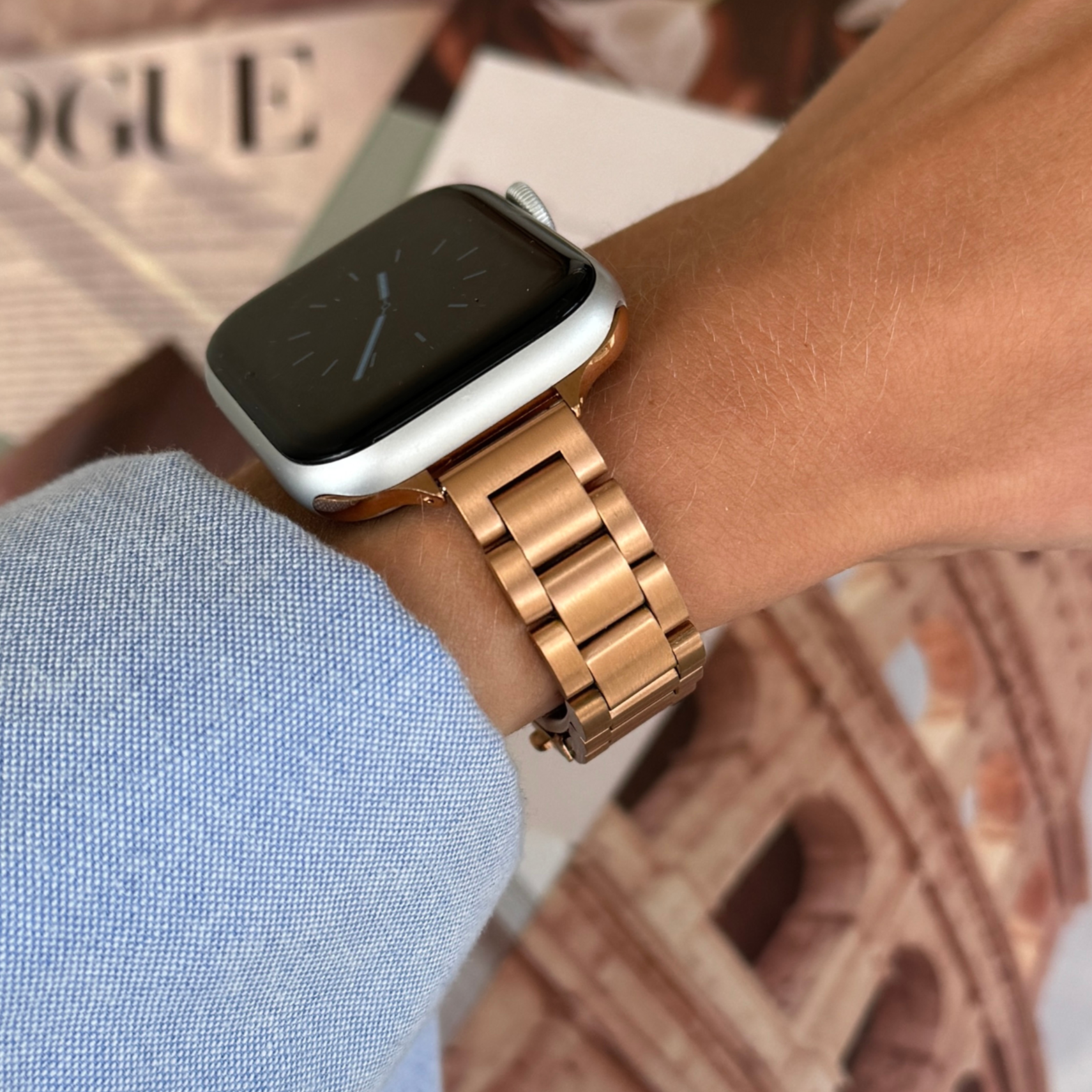 Rose gold slim link Apple Watch band worn on a wrist beside a fashion magazine, stainless steel strap for Apple Watch 38mm to 49mm