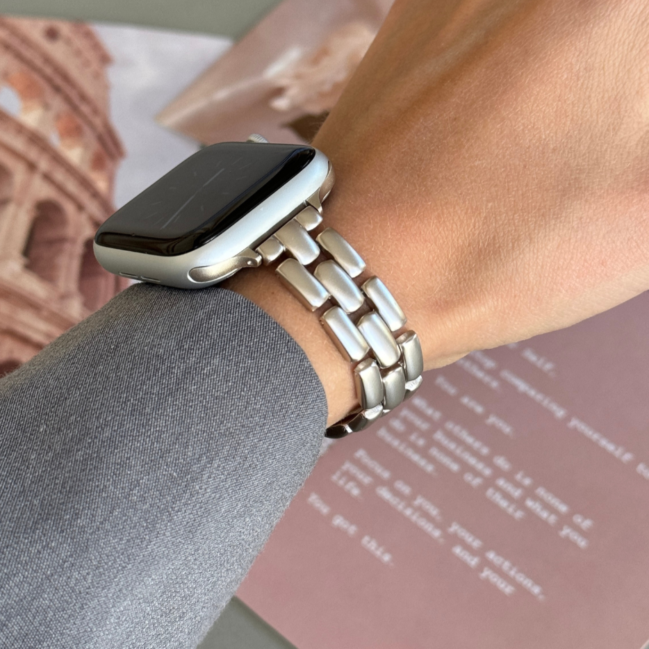 Starlight slim link Apple Watch band worn on a wrist beside a travel poster, metal strap for Apple Watch 38mm to 49mm