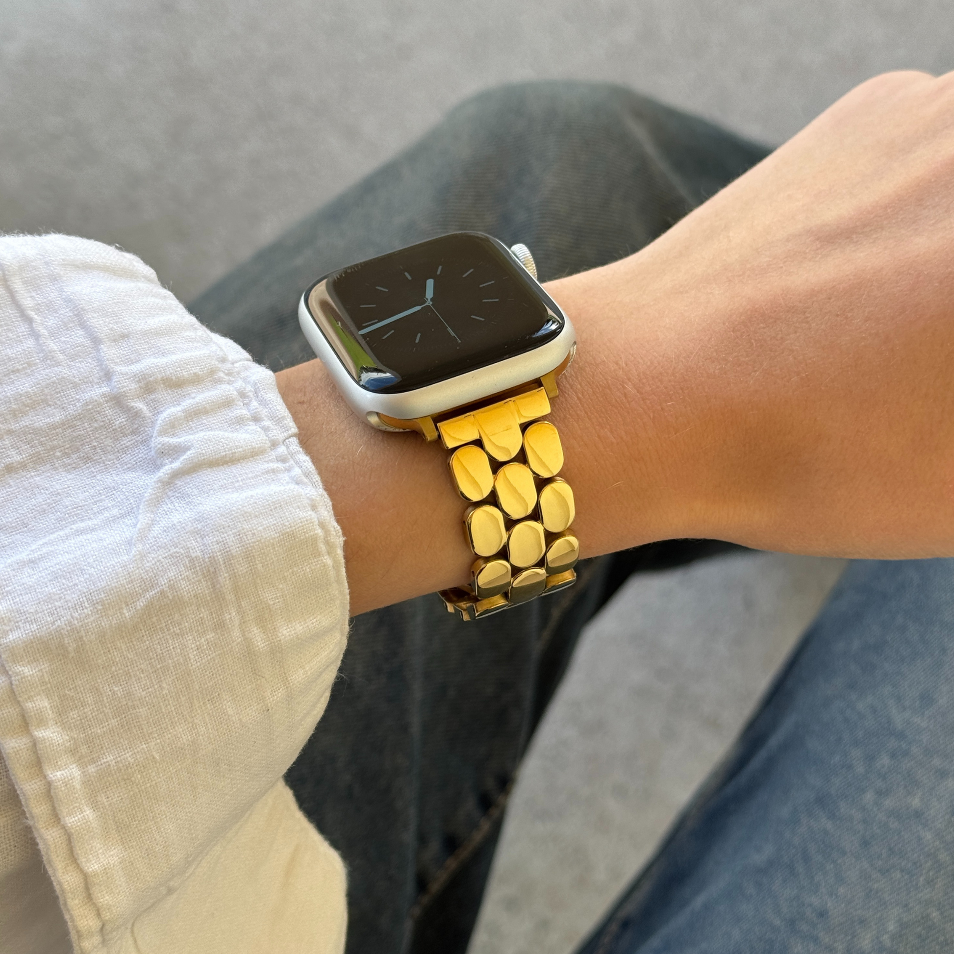 Smartwatch with a gold band on a wrist, wearing a white shirt and gray pants.