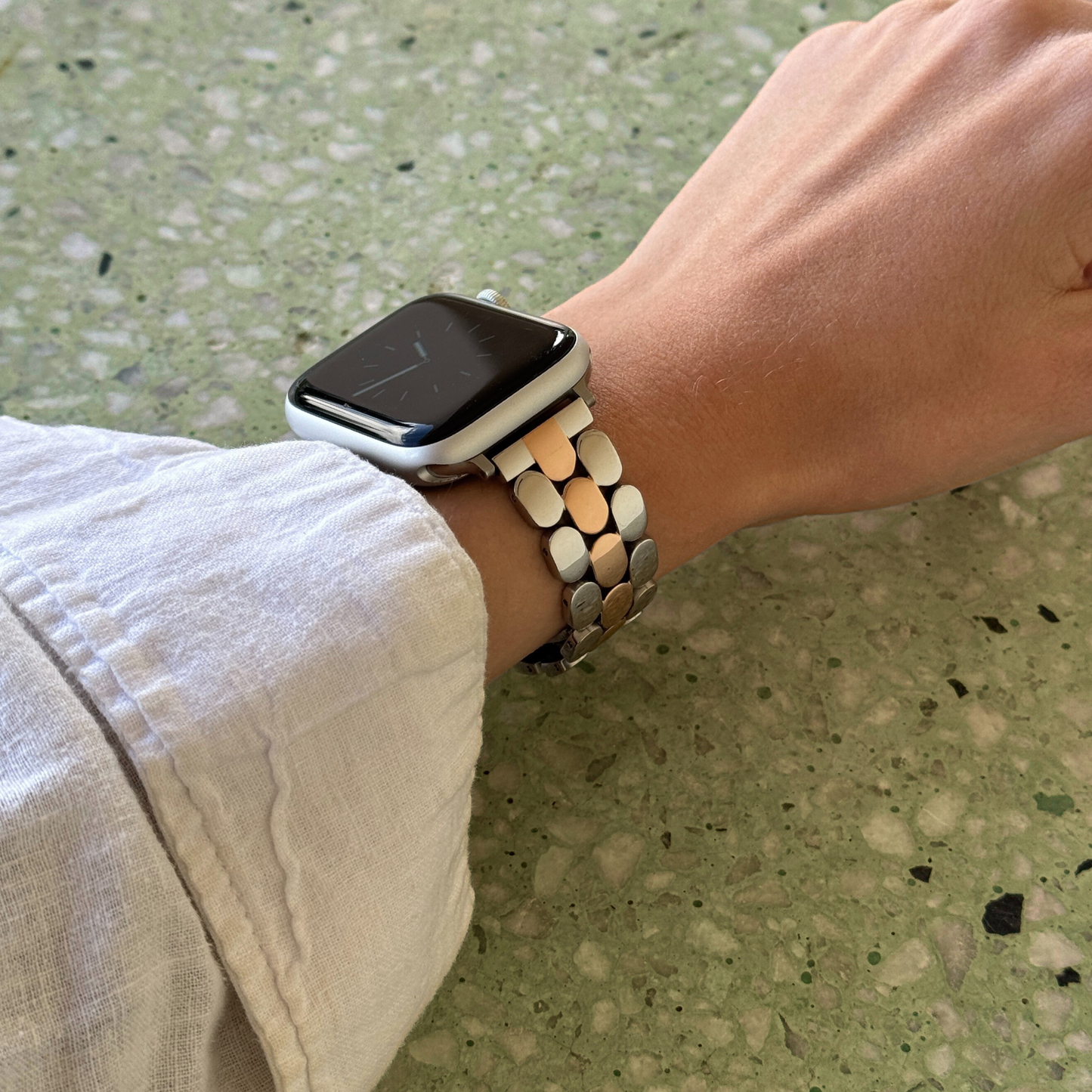 Smartwatch with a metallic band on a wrist against a textured green background