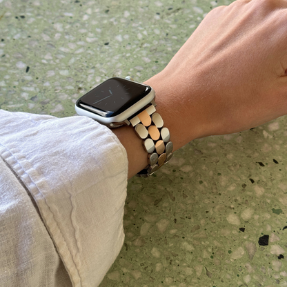 Smartwatch with a metallic band on a wrist against a textured green background