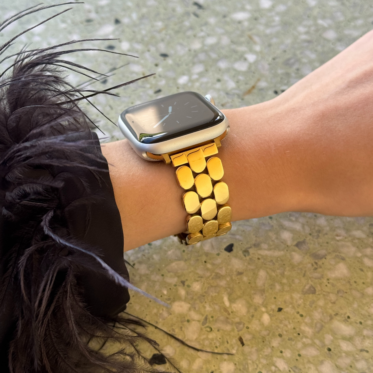 Person wearing a smartwatch with a gold band on a textured surface