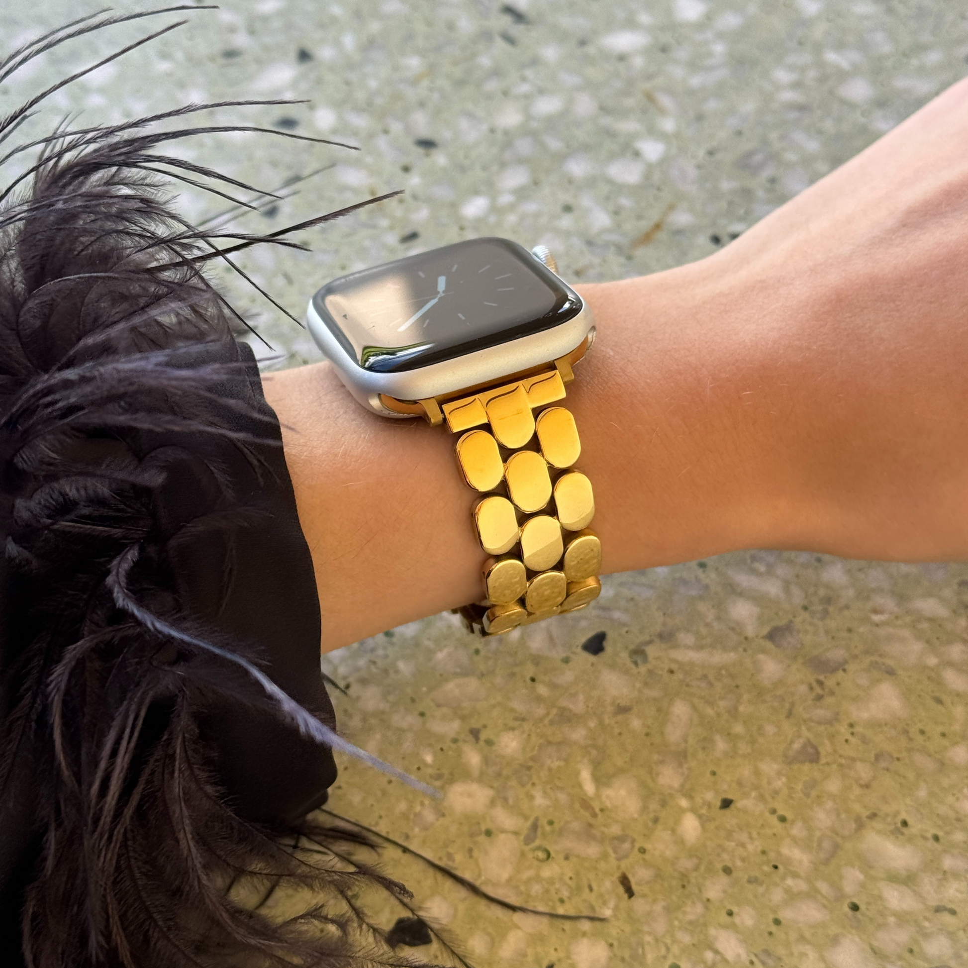 Person wearing a smartwatch with a gold band on a textured surface