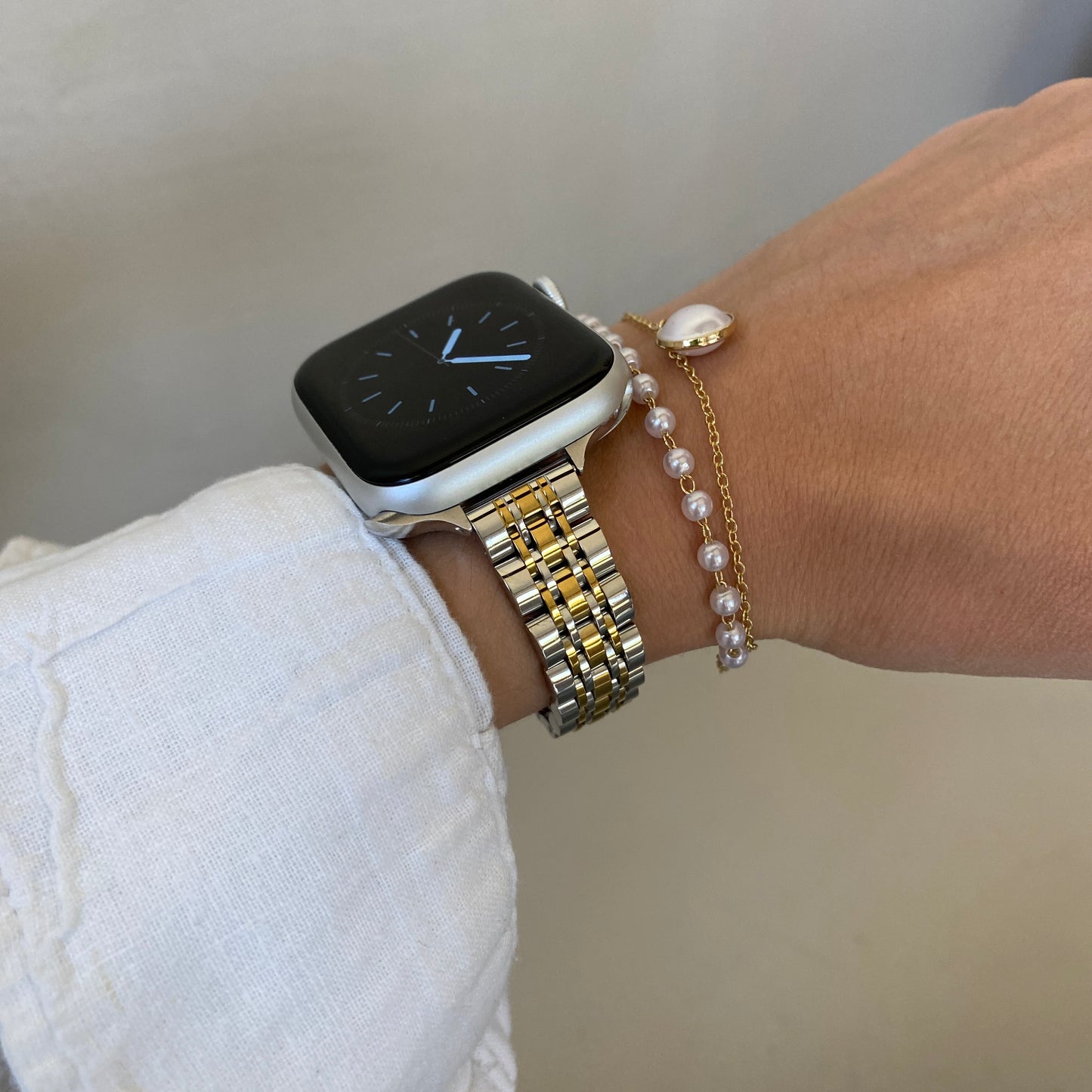 Smartwatch on a wrist with gold and silver bracelet and pearl bracelet against a neutral background