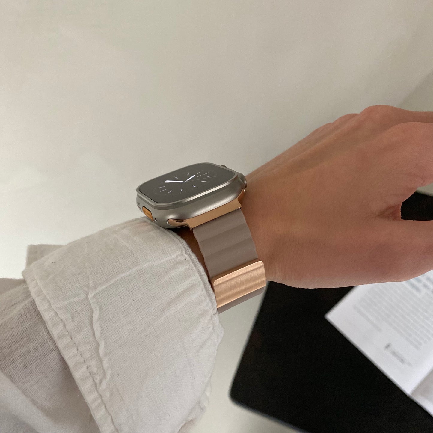 Person wearing a smartwatch with a gold band on a neutral background