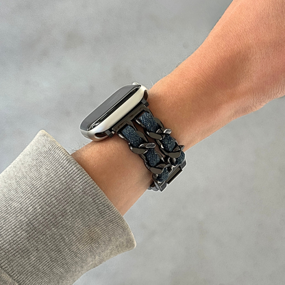 A close-up of a person's wrist wearing a black metallic chain link Apple watch band with a textured blue denim fabric inner lining, paired with a smartwatch.
