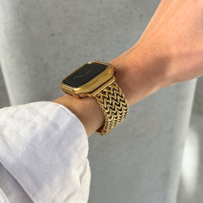 A close-up of a person's wrist wearing a gold-toned Apple smartwatch with a woven mesh band and a matching gold bezel, set against a light gray background.