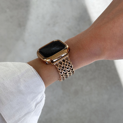 A close-up of a person's wrist wearing a rose gold-toned Apple smartwatch with a matching metallic mesh band and bezel, set against a soft gray concrete background.
