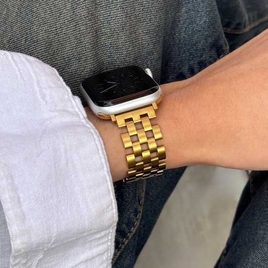 Smartwatch with a gold band on a wrist, wearing a white shirt and blue jeans.