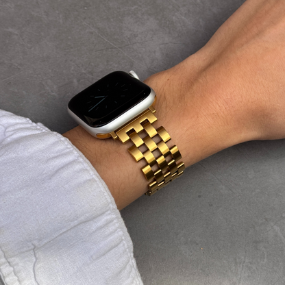 Smartwatch with a gold bracelet on a wrist against a gray background