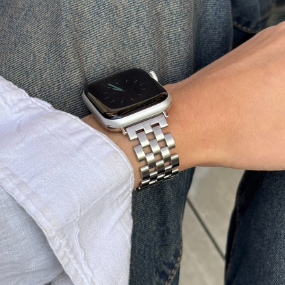 Smartwatch with a metal band on a person's wrist, wearing a white shirt and blue jeans.