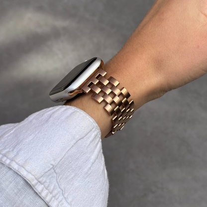 Person wearing a smartwatch with a rose gold metal band on a gray background