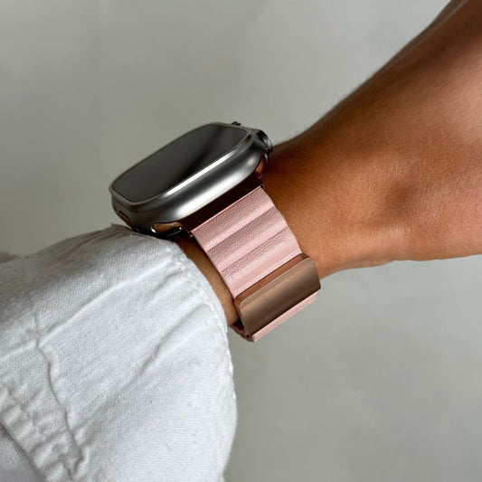 Person wearing a smartwatch with a rose gold band on a neutral background